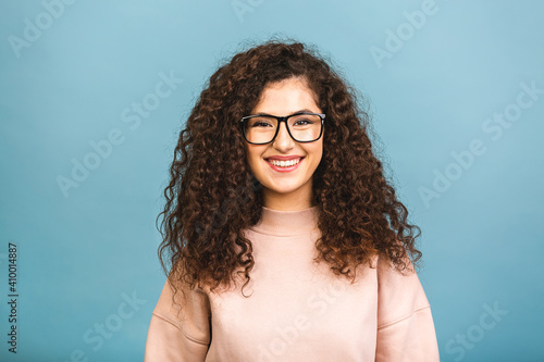 Portrait of a pretty smiling curly young woman in casual posing isolated on a blue background. © denis_vermenko