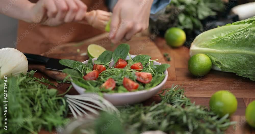 Housewife squeezing lemon juice on the salad, preparing healthy food on the kitchen table with green veggie ingredients. Close-up slow motion shot Housewife squeezing lemon juice on the salad, preparing healthy food on the kitchen table with green veggie ingredients. Close-up slow motion shot