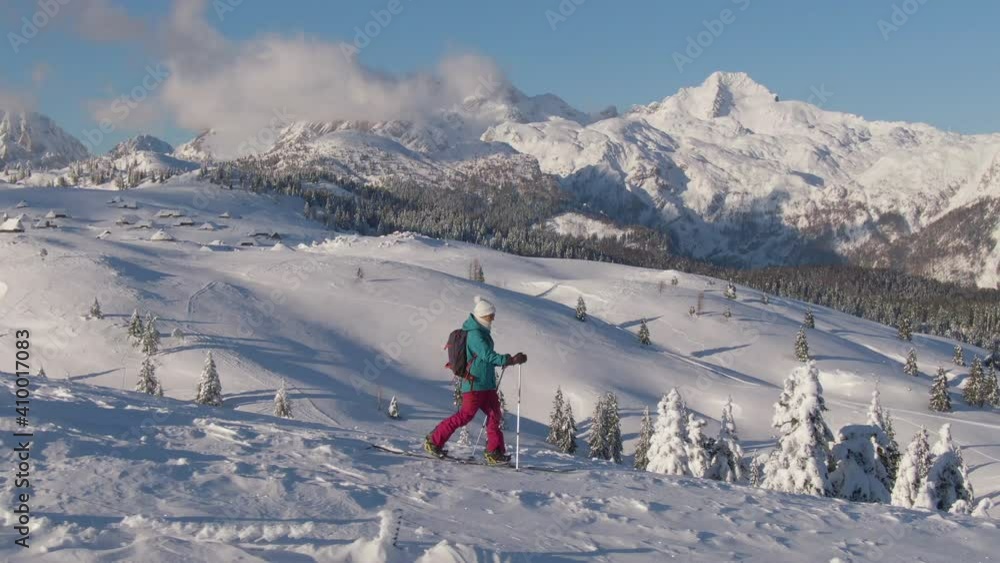 AERIAL: Young female tourist hikes down a snowy hill during a ski touring trip to scenic Velika Planina, Slovenia. Splitboarder explores the picturesque Slovenian mountains on a sunny winter day. AERIAL: Young female tourist hikes down a snowy hill during a ski touring trip to scenic Velika Planina, Slovenia. Splitboarder explores the picturesque Slovenian mountains on a sunny winter day.