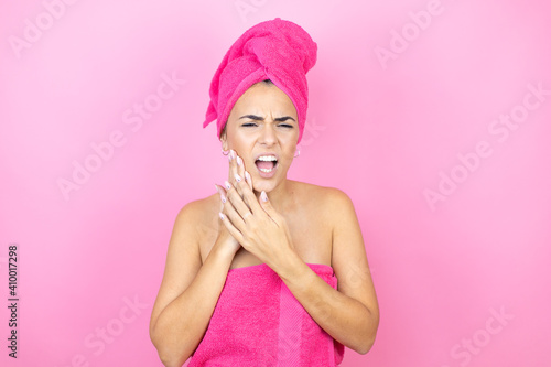 Young beautiful woman wearing shower towel after bath standing over isolated pink background touching mouth with hand with painful expression because of toothache or dental illness on teeth