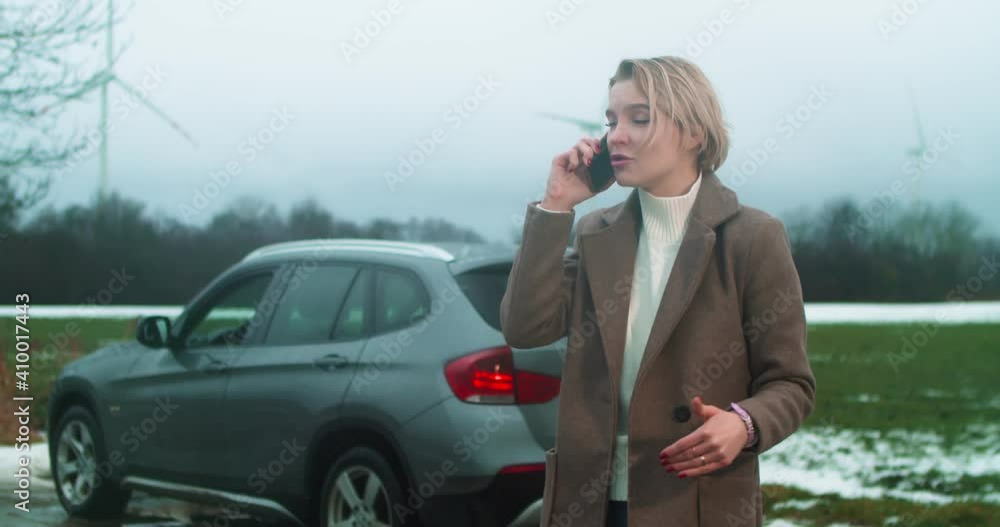 A beautiful business lady is nervously talking on the phone because of a problem with a car on the road. Pretty young woman nervously talks on the phone standing near a broken-down car A beautiful business lady is nervously talking on the phone because of a problem with a car on the road. Pretty young woman nervously talks on the phone standing near a broken-down car