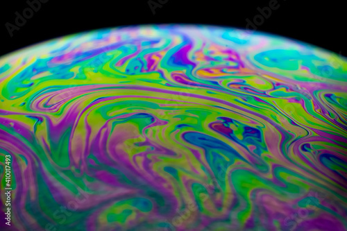 Close up, macro shot of a rainbow, multi colored soap bubble with yellow, purple, pink, blue and green colors on black background. 