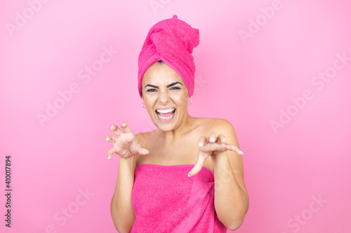 Young beautiful woman wearing shower towel after bath standing over isolated pink background smiling funny doing claw gesture as cat, aggressive and sexy expression