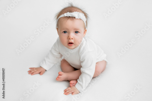 The child just learned to sit. A child on a white background looks up his mouth open. Cute little baby girl. A healthy infant with two teeth. Baby care and care. Interested in the surrounding worlds.