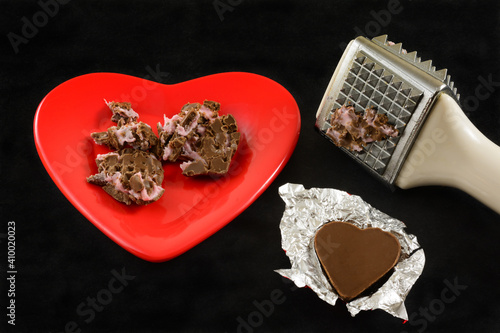 Crushed shredded chocolate heart with pink filling and meat tenderizer mallet and chocolate heart in foil as anti-Valentine symbol of divorce or broken heart photo