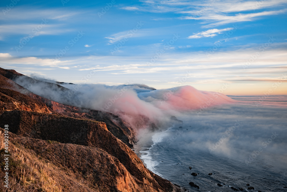 Scenic view of ocean shore near Big Sur, California, USA. Cloud covered coast, sea and cliff hills. Foggy pink sunset landscape.