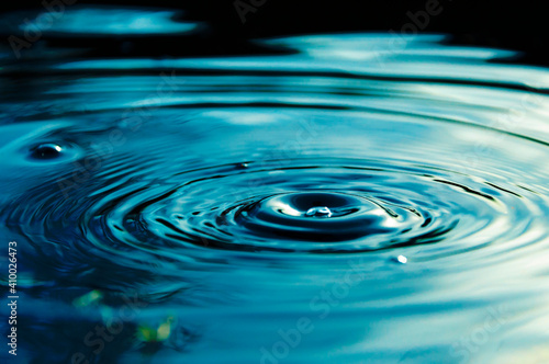 Circular waves and ripples in the water from a drop falling. Natural background blue water with circles and sky reflection.