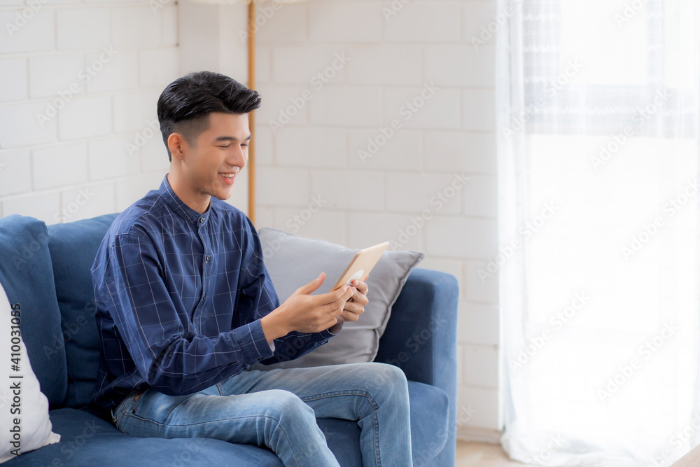 Young attractive asian man resting using browsing tablet computer on sofa at home, happy male sitting on couch relax reading digital gadget at house, communication and lifestyle concept. Young attractive asian man resting using browsing tablet computer on sofa at home, happy male sitting on couch relax reading digital gadget at house, communication and lifestyle concept.