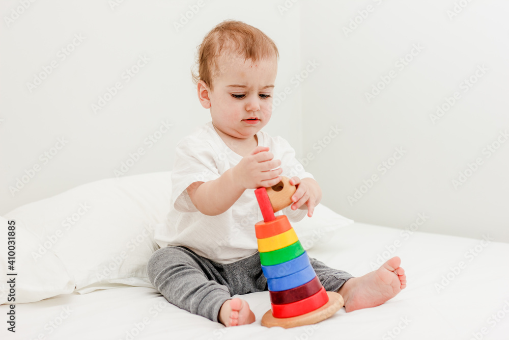 Cute baby boy playing colorful pyramid tower on white bed Cute baby boy playing colorful pyramid tower on white bed