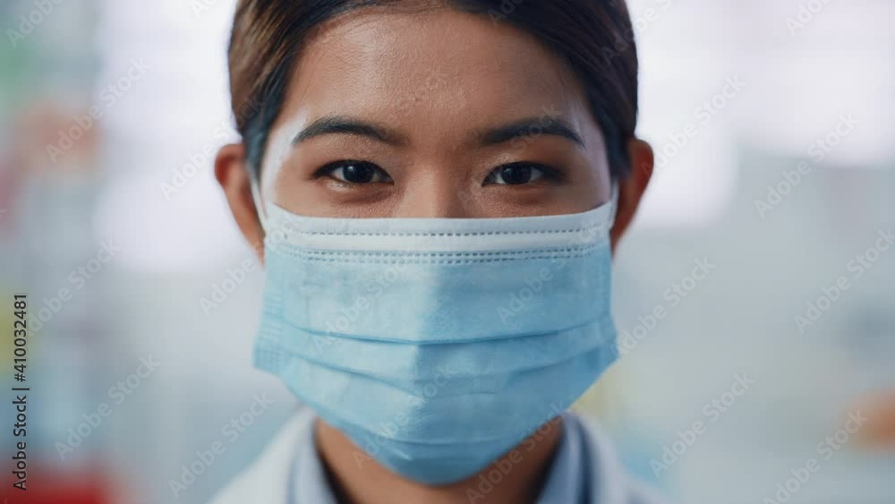 Beautiful Female Specialist Wearing Face Mask Looks Confidently at the Camera. Asian Woman with Amazing Dark Eyes and Black Hair Looks Ahead to the Bright Future. Blurred Bright Background Beautiful Female Specialist Wearing Face Mask Looks Confidently at the Camera. Asian Woman with Amazing Dark Eyes and Black Hair Looks Ahead to the Bright Future. Blurred Bright Background