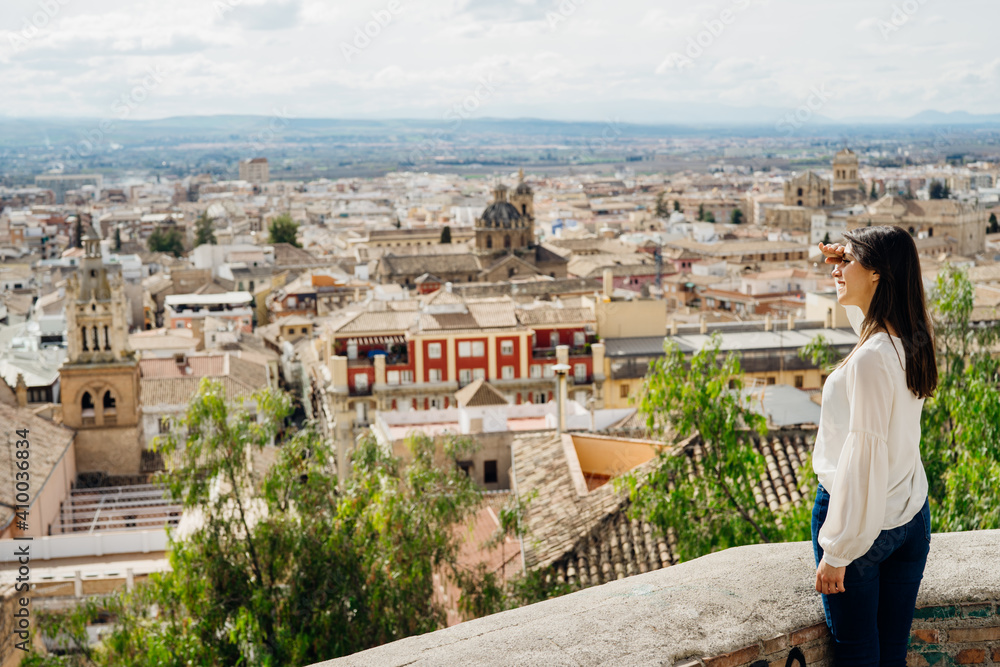 Young Spanish tourist woman on a day trip visiting Granada, Spain. Enjoying sightseeing experience in city center viewpoint.Popular cityscape observation location.Travel destination in Andalusia.