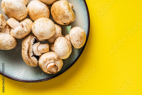 Top view on plate with white common champignon mushrooms on yellow background