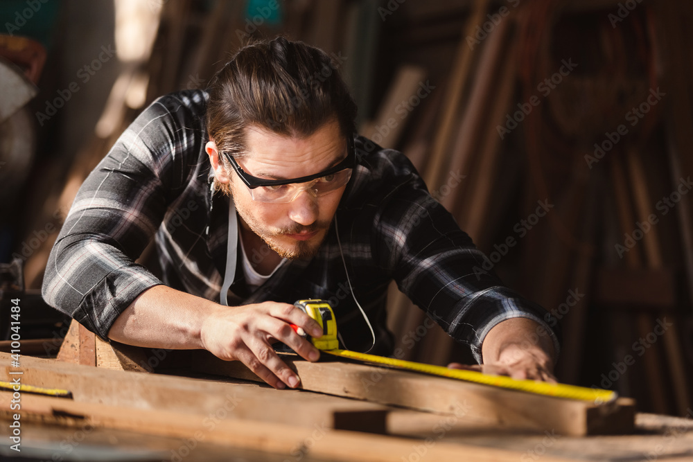 young carpenter caucasian man using measuring tape looking wood size at workspace. craftsman profession in wood factory.