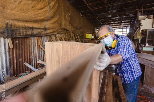 asian senior man carpenter wear protective mask dust and headphone working to measure size of wood. In his own woodworks.
