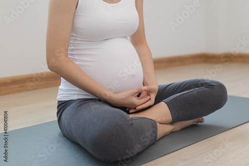 Calm pose young asian pregnant woman practice yoga in the lotus position for pregnant to meditation and exercise on mat for wellbeing while rest at home.