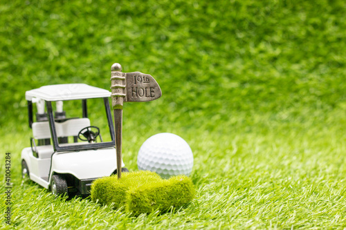 Golf 19th hole with golf cart and ball are on green grass