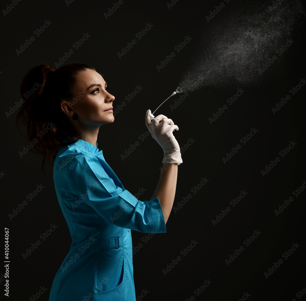 Obraz premium Pretty brunette woman doctor gynecologist nurse in latex gloves and medical uniform gown uses disinfectant spray medicine over dark background. Gynecology, healthcare, medicare concept