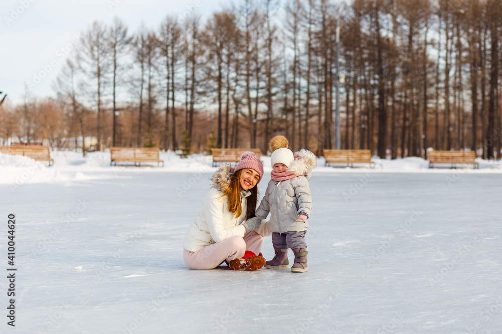 Obraz premium Happy young woman and one-and-a-half-year-old girl in winter in warm jackets walk in the park. mother and daughter in winter clothes