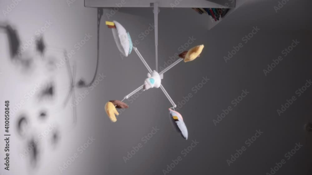 Baby's Colorful Mobile Toy Hanging And Spinning Over Baby Bed On Wall Background. - Low Angle Shot Baby's Colorful Mobile Toy Hanging And Spinning Over Baby Bed On Wall Background. - Low Angle Shot