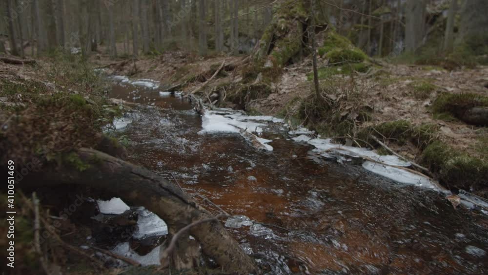 Low tracking shot over bubbling stream with snow flowing in national park in Finland Low tracking shot over bubbling stream with snow flowing in national park in Finland