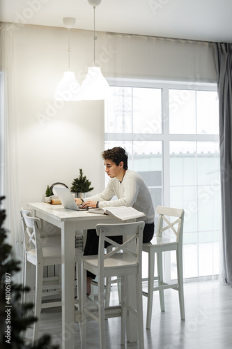 Concentrated young man working on laptop computer at home bright kitchen © Olga Gimaeva