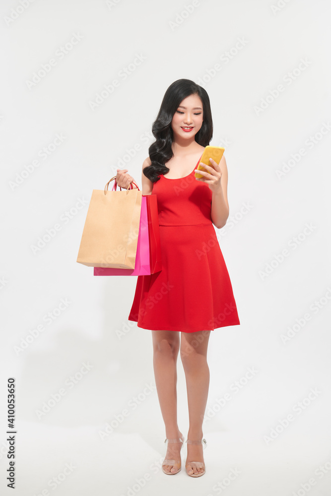 Lovely young girl wearing dress standing with colorful shopping bags and looking at mobile phone Lovely young girl wearing dress standing with colorful shopping bags and looking at mobile phone