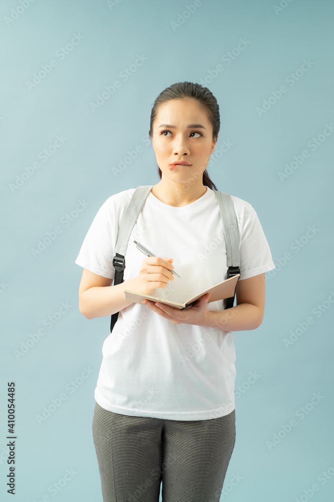 Puzzled indecisive troublesome college student frowns face in displeasure, diary in hands, thinks about writing new essay