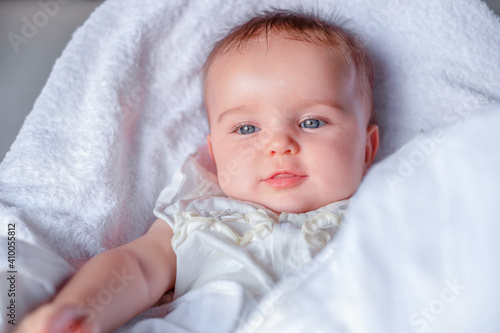 The baby lies and smiles in a white blanket © Vasleriia Kuznetsova