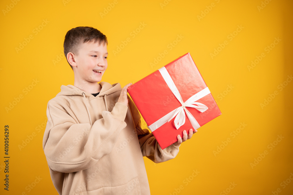 Cute boy holding big red gift box on yellow background. Celebrate new year, valentines day. Birthday gift. Birthday boy. Buy gifts. Cute boy holding big red gift box on yellow background. Celebrate new year, valentines day. Birthday gift. Birthday boy. Buy gifts.