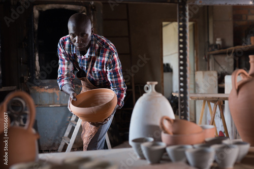Canvas Print Positive african potter enjoying work, checking ceramic products in pottery stud