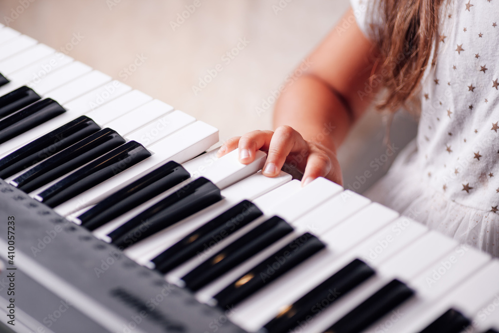 Fototapeta premium close-up portrait, insecure childish hand of a girl with long hair in a white dress learning music on an electronic synthesizer in the living room.