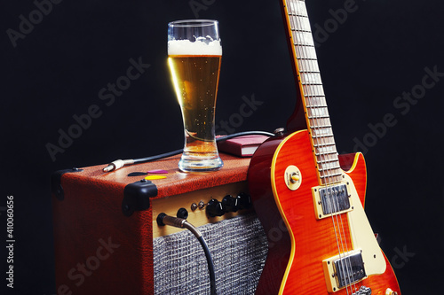 Tube combo amplifier for guitar with guitar, glass of beer and notepad on black background.