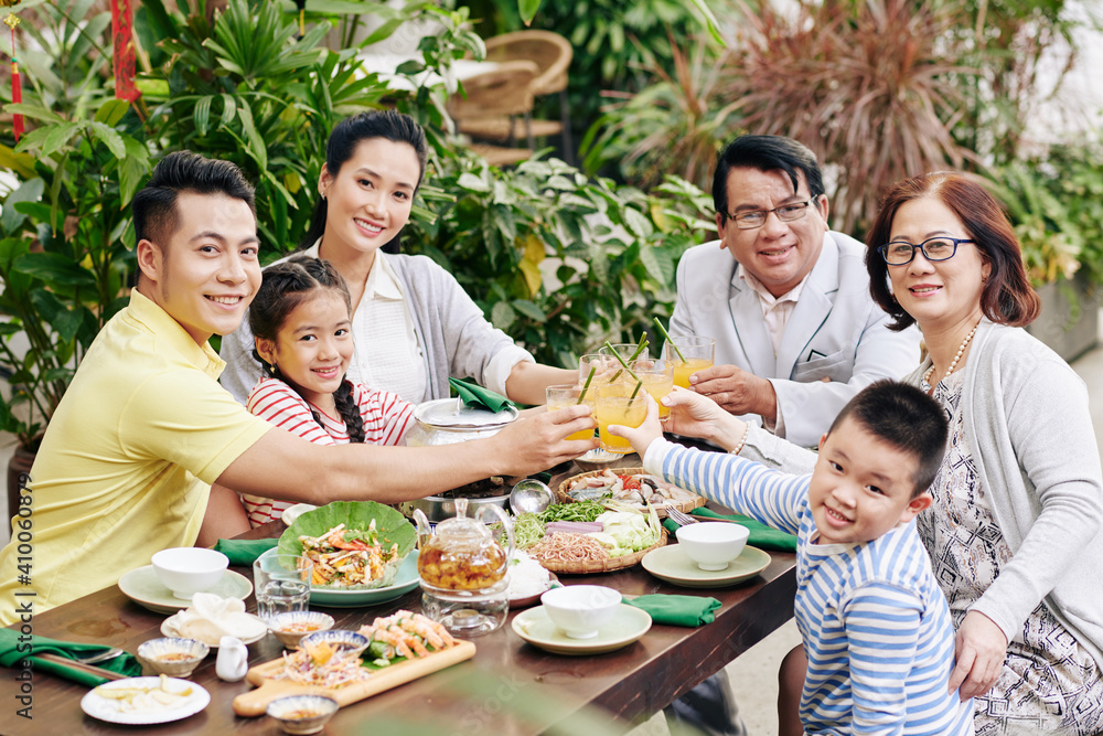 Big happy Asian family toasting with glasses of orange juice when sitting at big dinner table and celebrating spring festival Big happy Asian family toasting with glasses of orange juice when sitting at big dinner table and celebrating spring festival