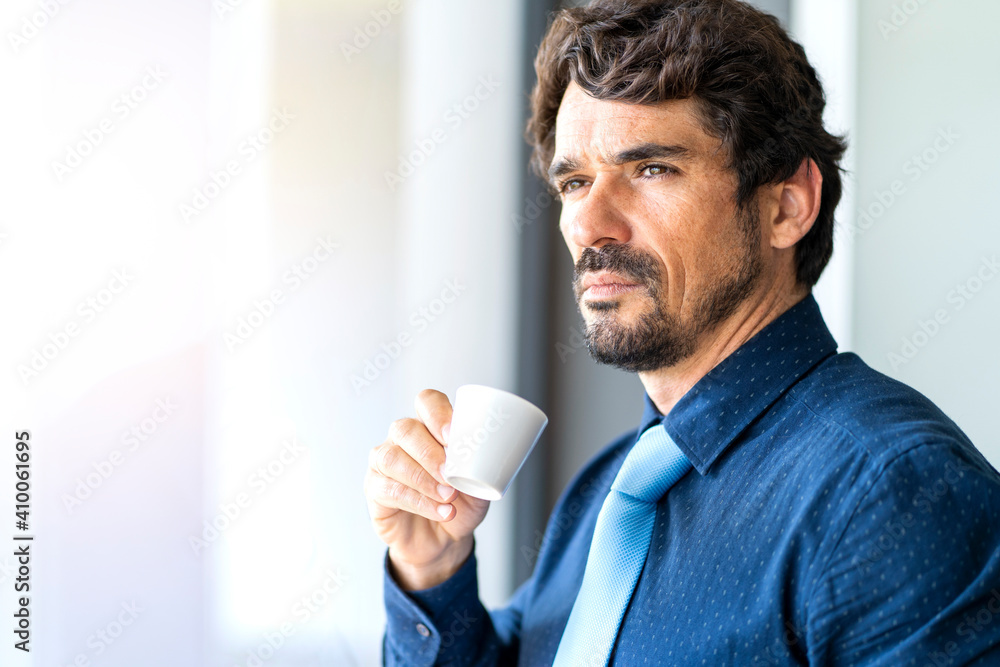 Business man smiling and looking through the window holding a cup of coffee. Success man portrait with serious face Business man smiling and looking through the window holding a cup of coffee. Success man portrait with serious face
