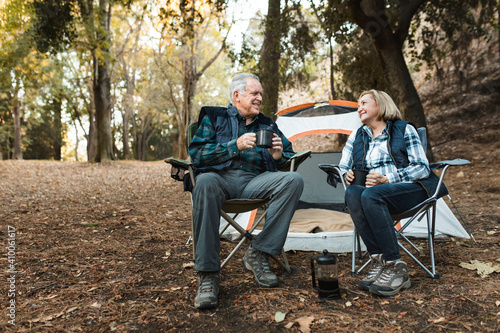 Happy retired couple having coffee by the tent in the forest