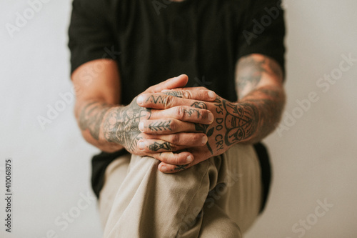Tattooed man with hands clasping his knees