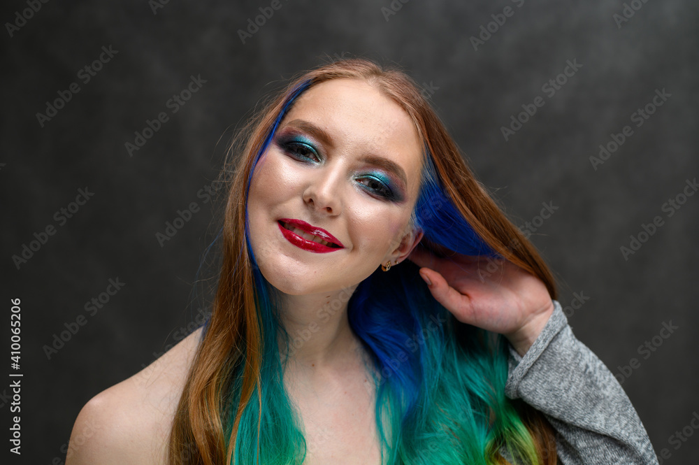 Fototapeta premium Photo of a happy woman. Portrait of a beautiful caucasian girl with dyed hair and excellent makeup on a gray background.