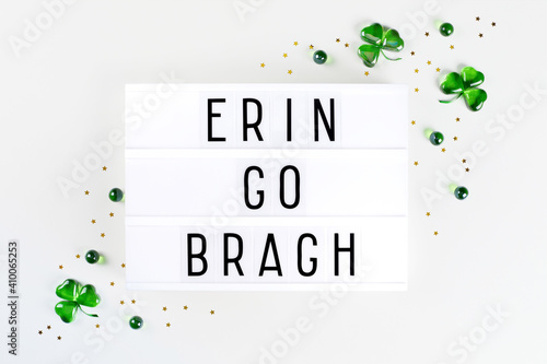 Lightbox with text Ireland forever written in Irish and shamrock symbols made of green hearts and stars confetti on white background. Flat lay Irish holiday card Spring 17 march lucky clover design. photo