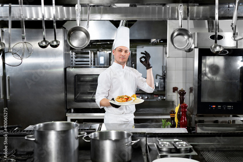 Chef in the restaurant holds a plate with a ready-made dish and shows the   OK   sign