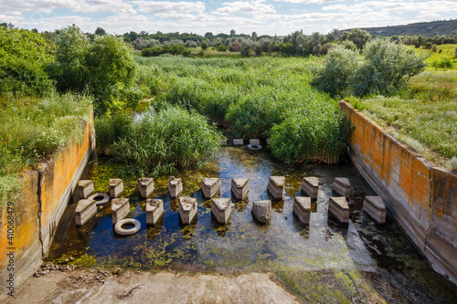 Concrete breakwaters in bottom of discharge sluice in earthen dam on small river. Hydraulic structure for protecting ground from erosion