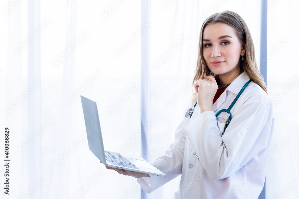 female doctor with stethoscope working with laptop computer and writing on paperwork on wooden table in Hospital background female doctor with stethoscope working with laptop computer and writing on paperwork on wooden table in Hospital background