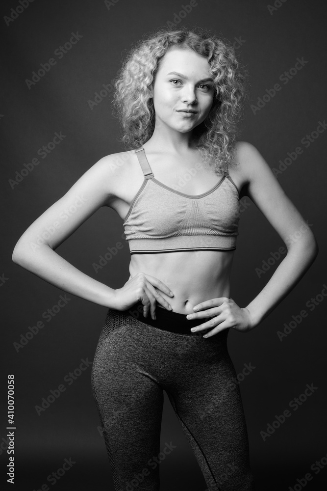 Young beautiful woman with curly blond hair ready for gym against gray background Young beautiful woman with curly blond hair ready for gym against gray background