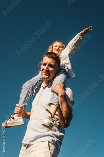 Piggyback of girl and her dad, bottom view. Blue sky background. Freedom concept and happiness.