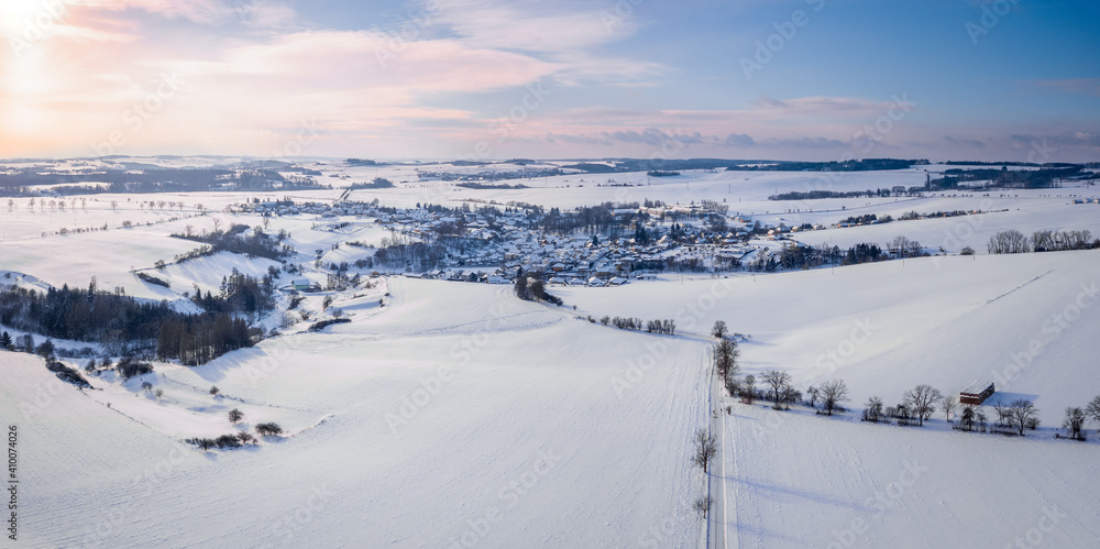 Aerial view of landscape with village Puklice, residential buildings in winter. Winter landscape snow covered field and trees in countryside. Czech Republic Highland
