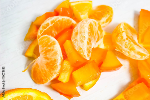 Sliced slices of tangerine, orange and persimmon on a white background.