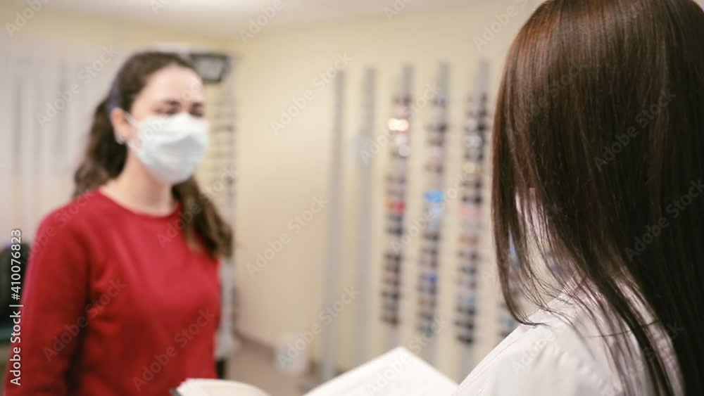 A woman in a medical mask, dressing gown and gloves, shows a jar of medicines. In the background, glass cases with medicines. Concept of a viral pandemic and protection against infection A woman in a medical mask, dressing gown and gloves, shows a jar of medicines. In the background, glass cases with medicines. Concept of a viral pandemic and protection against infection