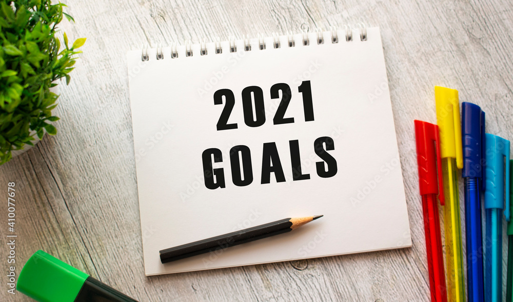 A notebook on a spring with the text 2021 GOALS lies on a wooden table with colored pens. A notebook on a spring with the text 2021 GOALS lies on a wooden table with colored pens.