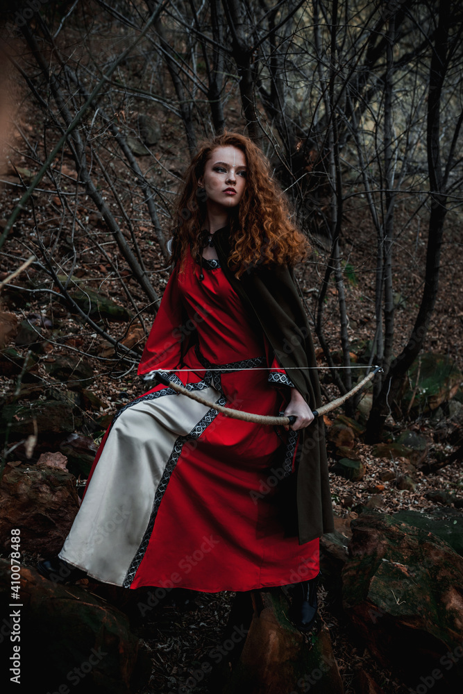Red-haired woman in a red dress in a historical Celtic costume in the autumn forest Red-haired woman in a red dress in a historical Celtic costume in the autumn forest