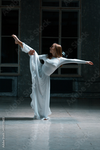 girl dancer doing stretching in a white dress in a dark room
