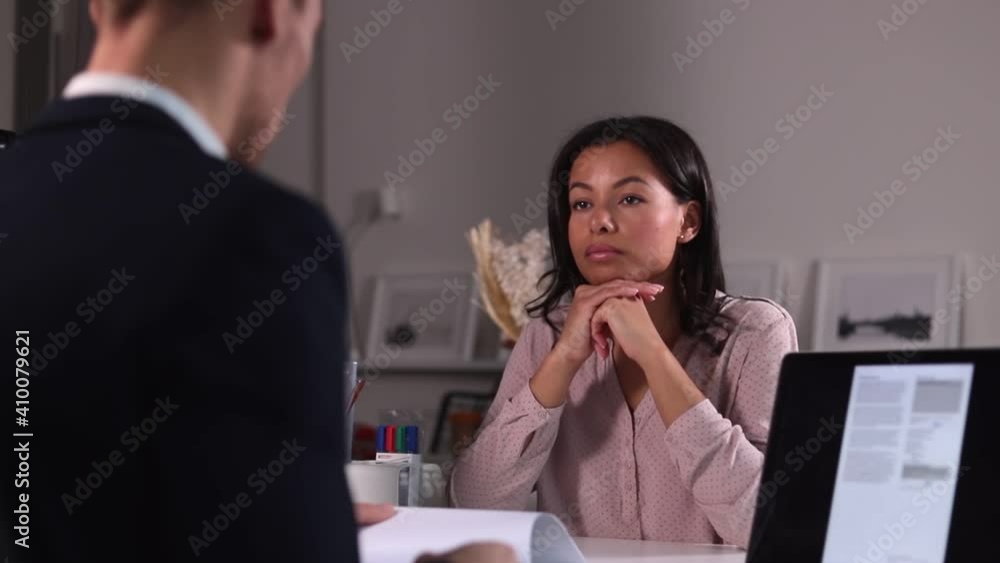 Man hr specialist talking to woman job seeker and sitting at table in modern office spbi. Beautiful young female candidate sits in front of businessman who reading paper resume at desk with computer Man hr specialist talking to woman job seeker and sitting at table in modern office spbi. Beautiful young female candidate sits in front of businessman who reading paper resume at desk with computer